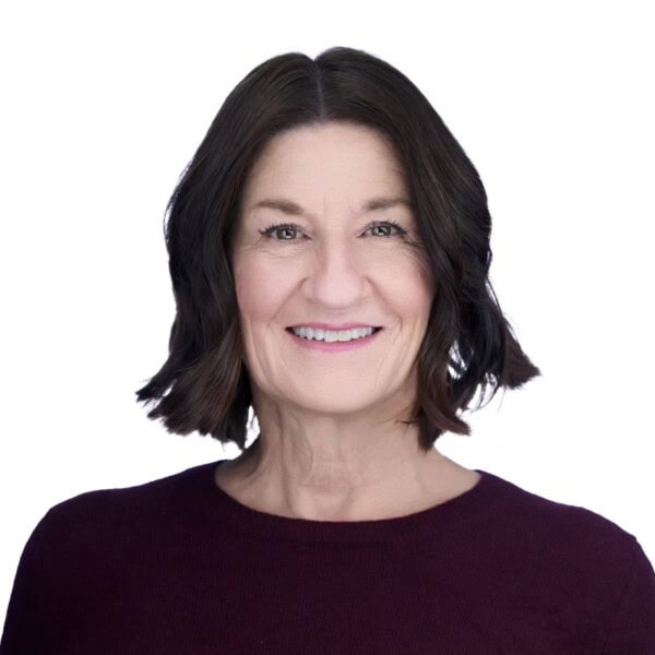 Smiling woman with short, dark brown hair wearing a dark burgundy top, posed against a plain white background.